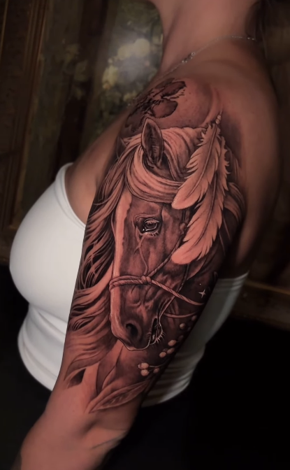 A detailed tattoo of a horse's head, featuring flowing mane and feathers, displayed on a person's upper arm.