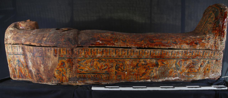 An ancient Egyptian wooden sarcophagus, richly decorated with intricate colorful paintings and hieroglyphics, laying on a display table.