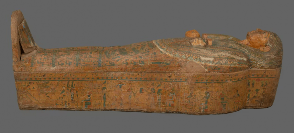 An ancient Egyptian sarcophagus with intricate painted decorations, featuring figures and hieroglyphics, lying on its side.