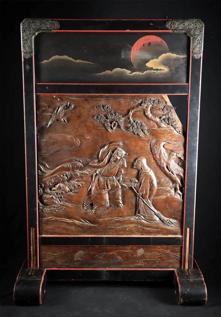 A decorative wooden panel featuring intricate carvings of two figures interacting, set against a backdrop of stylized waves and a red moon.