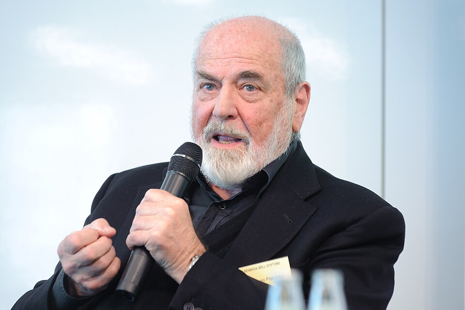 An older man with a beard speaking into a microphone during a panel discussion.