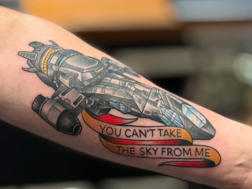 Jason Tritten tattooing a vibrant American Traditional Serenity spaceship from Firefly at Revolt Tattoos Fashion Show Mall Las Vegas