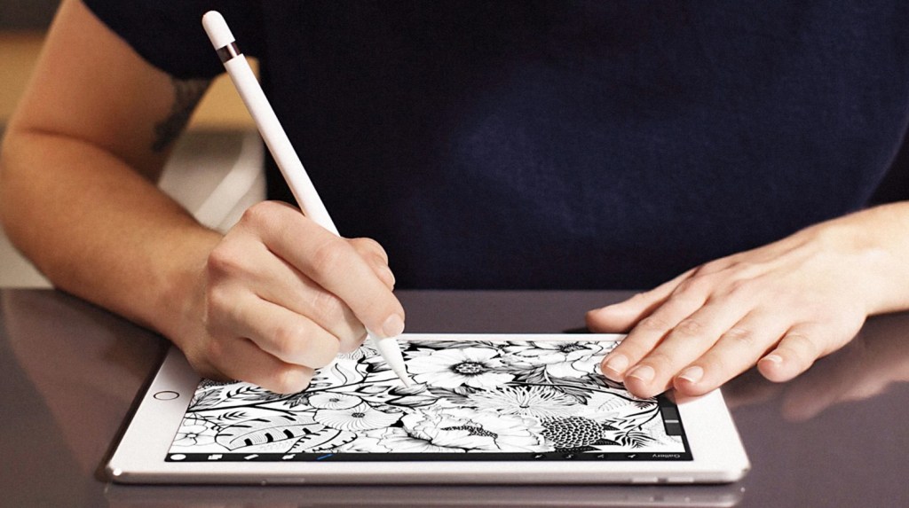 Close-up of a tattoo artist's hands drawing on a digital tablet with a stylus, surrounded by traditional tattoo reference sheets.