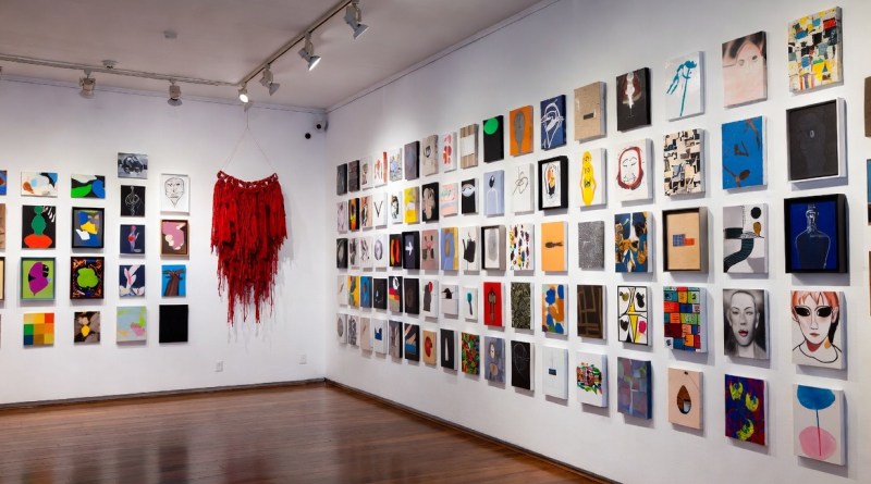 "AI-generated 16:9 illustration of the Art (by) Dealers exhibition installation at White Columns, showing colorful anonymous artworks in a salon-style hang."