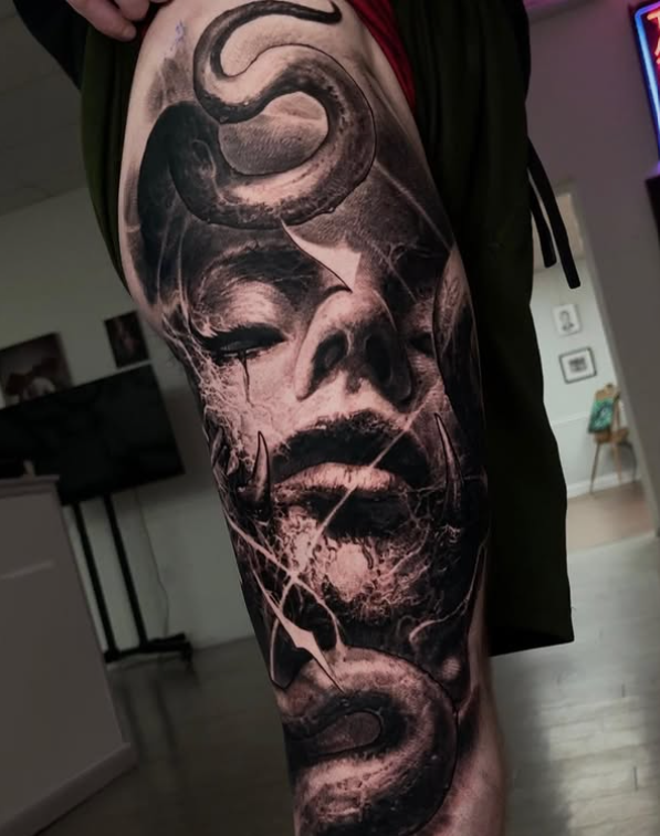A close-up of a detailed leg tattoo depicting a face with a snake intertwined, showcasing intricate artistic elements.