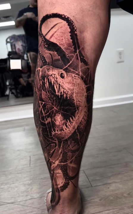 A detailed tattoo on the leg featuring a fierce-looking snake with bared teeth and intertwined octopus tentacles, set against a backdrop of abstract lines.