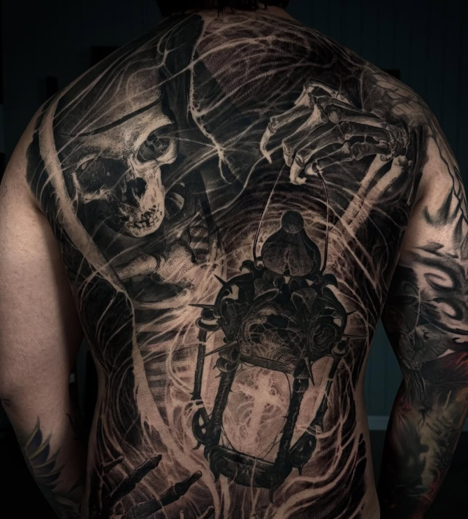 A detailed tattoo covering the back of a person, featuring a skull, a lantern, and skeletal hands, set against a dark background.