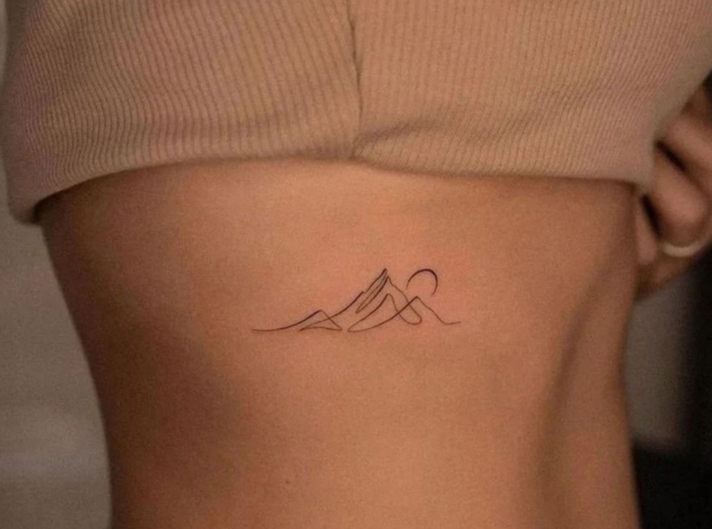 Minimalist mountain range tattoo with a sun, located on the side of a person's torso.