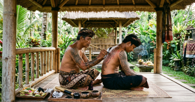 Tattoo artist hand-poking ink into a seated man's back in a bamboo pavilion