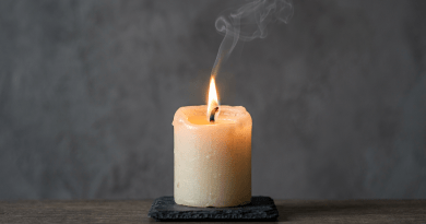 Lit beige candle on dark slate with curling smoke