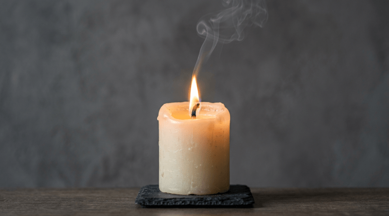 Lit beige candle on dark slate with curling smoke
