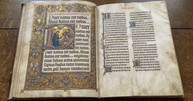 Open medieval illuminated manuscript with gold decorations and nativity illustration