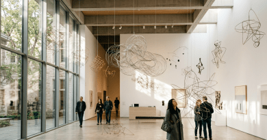Visitors observing hanging wire sculptures and framed artwork in a modern art gallery with large windows