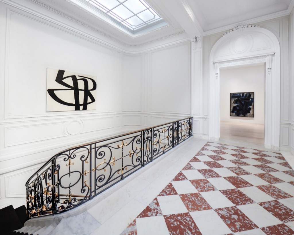 Elegant white-walled gallery interior with black abstract painting on the wall and checkered marble floor, showcasing Lévy Gorvy Dayan’s sophisticated exhibition space.

