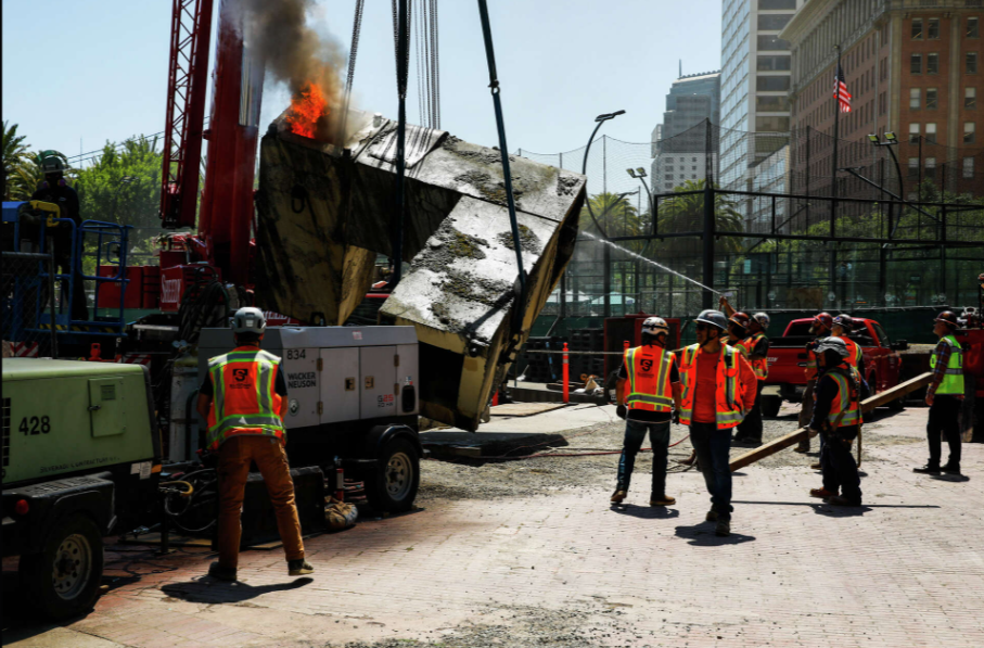 Firefighters and workers in safety vests spray water on a burning section of the Vaillancourt Fountain during its official dismantling in San Francisco.

