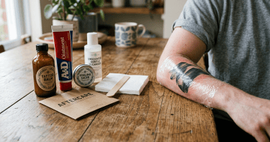 Fresh tattoo wrapped in plastic on arm beside tattoo aftercare products on wooden table