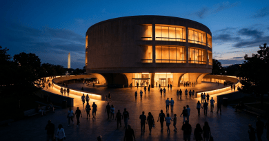 People walking around illuminated circular Kennedy Center building at dusk with Washington Monument visible