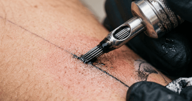 Tattoo machine needle applying black ink on human skin with gloves on hand