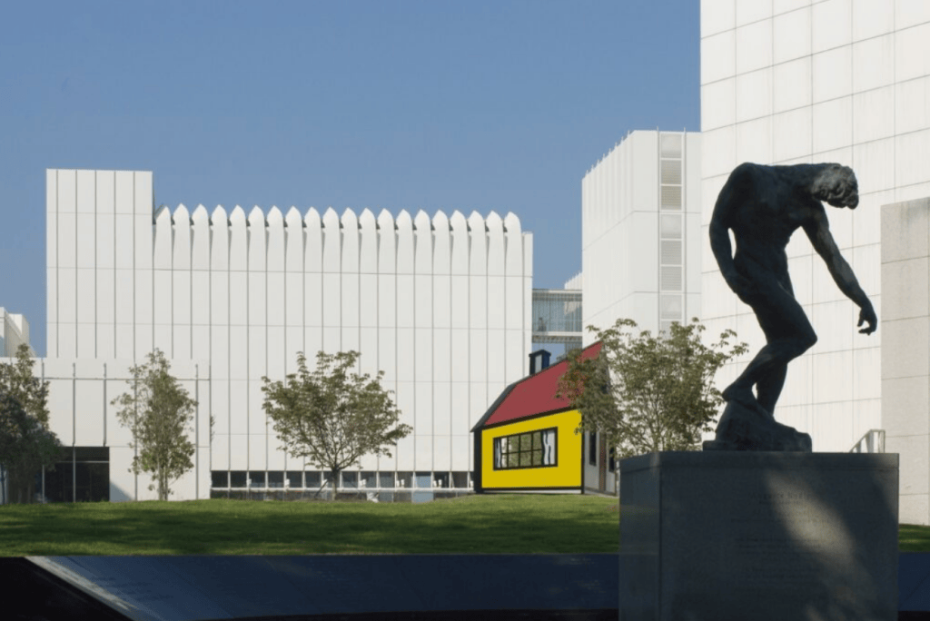Modern white architectural building of the High Museum of Art in Atlanta under a clear blue sky, featuring curved glass facades, elevated walkways, a large bronze sculpture in the foreground, and a bright yellow auxiliary structure, symbolizing the cultural landmark at the center of the embezzlement scandal.

