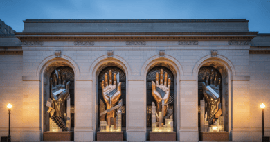 Four monumental abstract sculptures with hand motifs on a classical museum facade at dusk