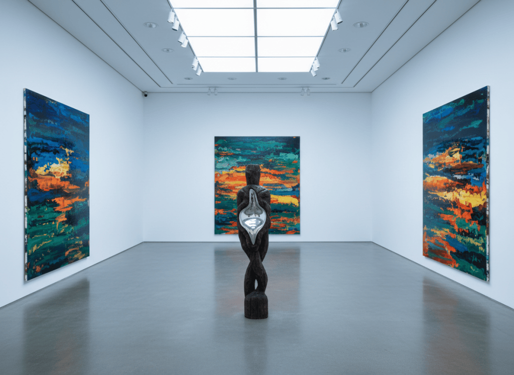 White-cube gallery with layered inkjet paintings and a wooden sculpture holding liquid metal.